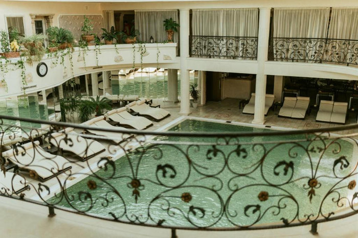 Piscina interioară privită de la etaj, printr-o balustradă din fier forjat, cu șezlonguri și plante agățătoare.