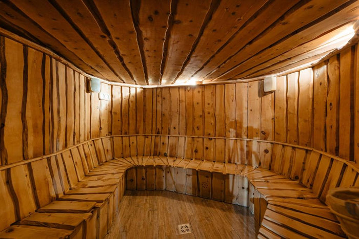 Saună rustică cu pereți din scânduri cu muchie naturală și bancă în semicerc, luminată discret pe sub tavan.