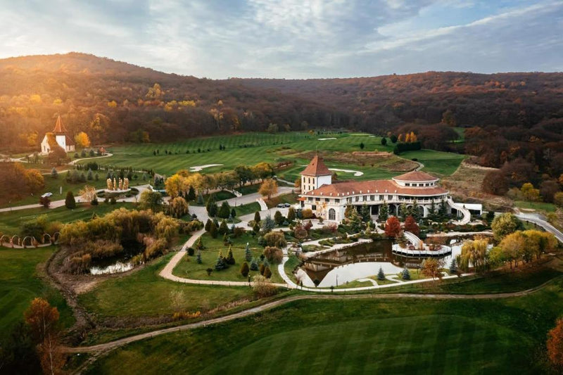 Vedere aeriană a resortului la apus, cu clădirea principală, lacul, terenul de golf și dealurile împădurite.