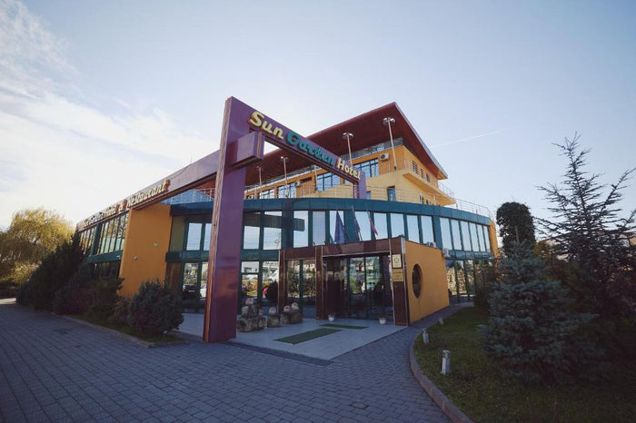 Fațada Sun Garden Hotel din Turda, cu firma de deasupra intrării, parter vitrat și alee pavată în față.